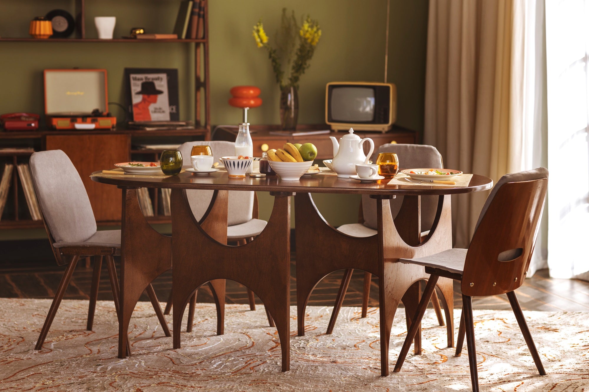 A cozy dining table set with plates, fruits, and drinks, surrounded by stylish chairs, against a retro decor backdrop.