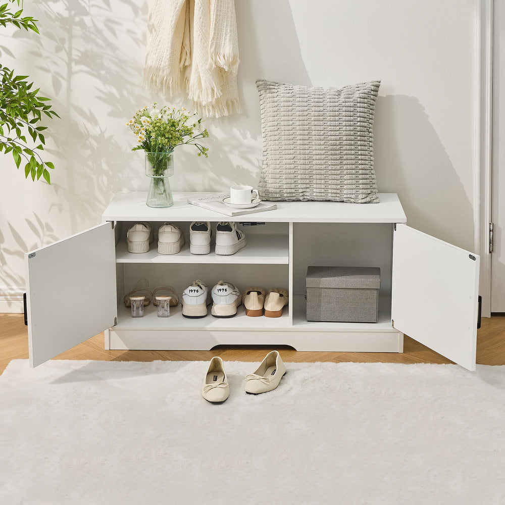 A stylish white storage bench with two black handles, adorned with a vase of flowers, a cushion, and a coffee cup on top.