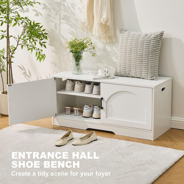 A white shoe bench in a foyer, featuring multiple shoes, a decorative vase with flowers, a cozy pillow, and a cup on top.