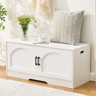 A stylish white storage bench with two black handles, adorned with a vase of flowers, a cushion, and a coffee cup on top.