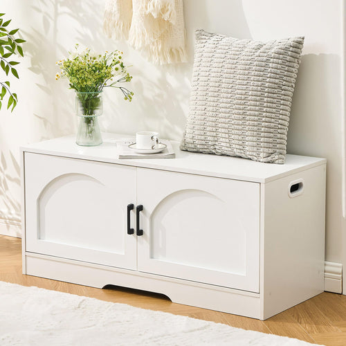 A stylish white storage bench with two black handles, adorned with a vase of flowers, a cushion, and a coffee cup on top.