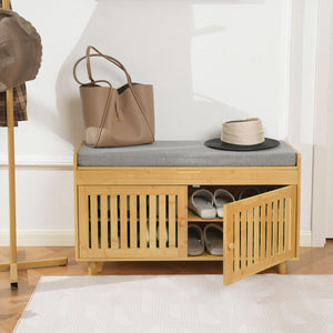 A stylish bamboo storage bench with a gray cushion, holding a brown handbag, a beige hat, and open to reveal neatly stored shoes.