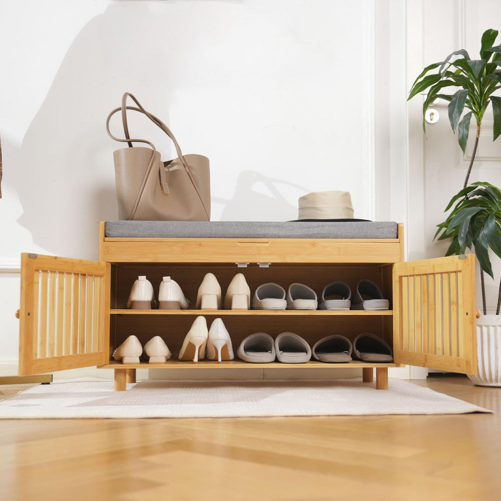 A stylish wooden bench with a gray cushion, a handbag, books, and a vase of flowers, placed near a door and slippers on the floor.