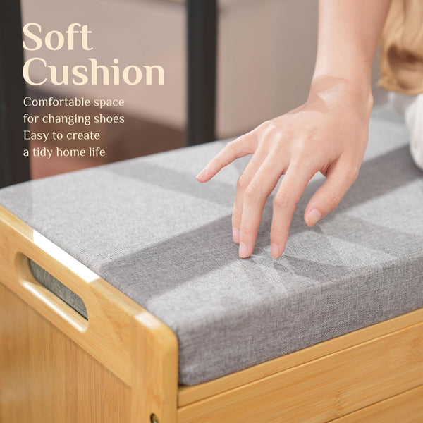 A hand gently touches a soft, gray cushion atop a bamboo storage bench, showcasing a cozy space for changing shoes.