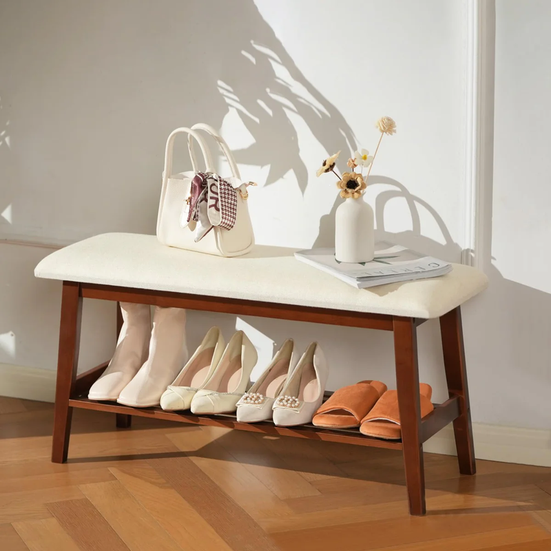 A stylish wooden bench displaying various elegant shoes, a sleek handbag, a vase with flowers, and a magazine in a sunlit room.