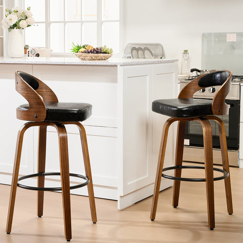 Two modern wooden bar stools with black leather seats are positioned at a kitchen island, featuring a vase of flowers and a fruit bowl.