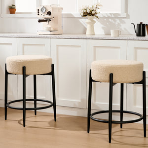 Two beige upholstered bar stools with black legs sit in a modern kitchen, adjacent to a coffee machine and decorative elements.
