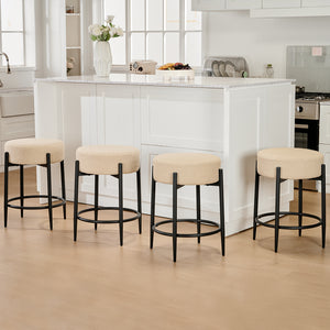 Four beige upholstered bar stools with black metal legs arranged neatly in a bright kitchen with white cabinetry and a marble countertop.