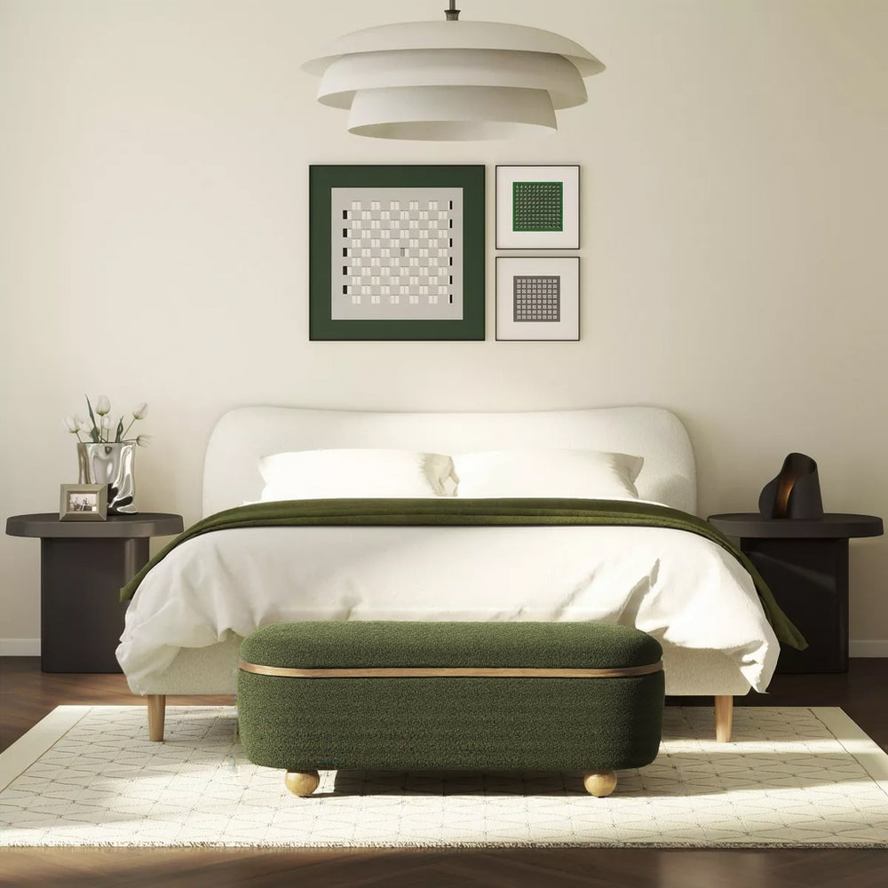 A plush green upholstered storage bench with rounded edges and wooden feet, next to a blurred figure walking in a minimalist setting.