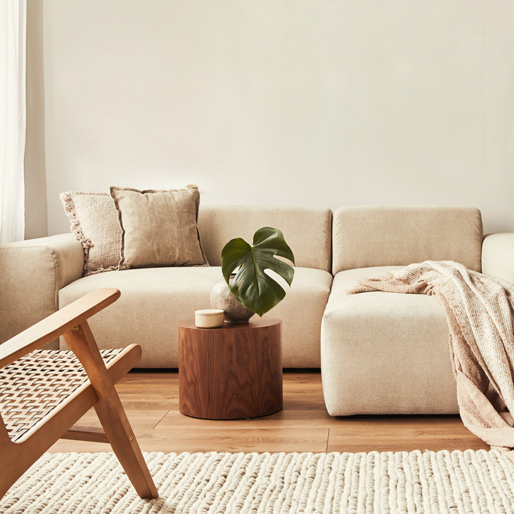 A cozy, neutral-toned living area featuring a plush sectional sofa, a wooden accent table with a plant, and a textured rug.